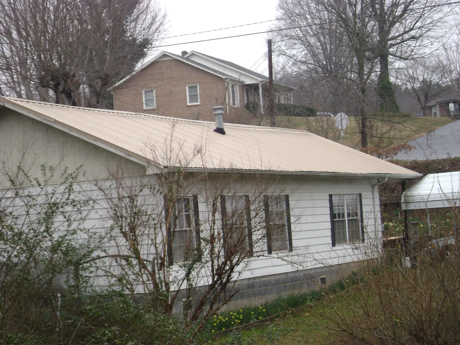Tan metal roof on a white sided house set into a hillside — Commercial Roofing by Roofing Brothers in Grass Valley